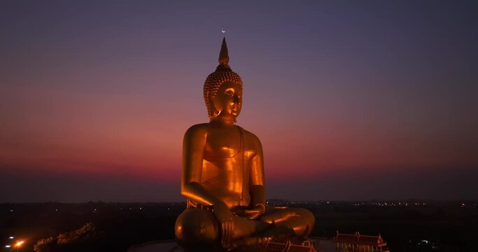 .aerial view The moon was above the head of the biggest golden Buddha in the world at twilight. .low night atmosphere golden big buddha was popular landmark and famous at wat Muang Ang Thong Thailand.