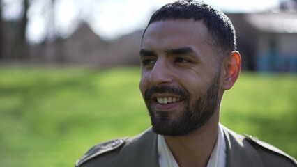 Portrait of a happy Middle Eastern young arab man looking at camera standing outside at park during sunny day