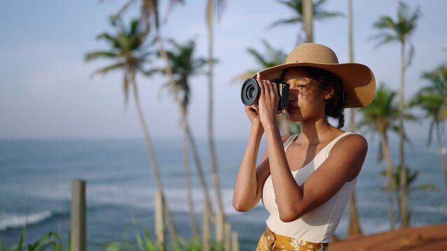 African american woman takes photos with camera on tropical island. Female multiracial photographer tourist explores ocean view location on vacation. Black girl taking pictures on sunrise.