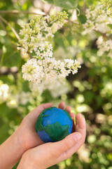 child holds a plasticine planet Earth against a background of flowers. Concept day earth, save environment.