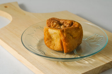 A piece of fried tofu is served on a small plate on a wooden cutting board isolated on a white background