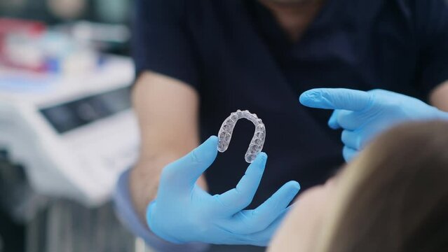 Orthodontist in rubber gloves holding transparent aligners for correction of dentition for patient closeup of innovative caps for teeth alignment in modern dentistry clinic