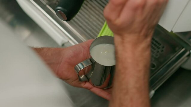 barista uses coffee machine and churns fresh milk to prepare latte or cappuccino in cafe for customer