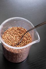 Buckwheat groats in a spoon on black background