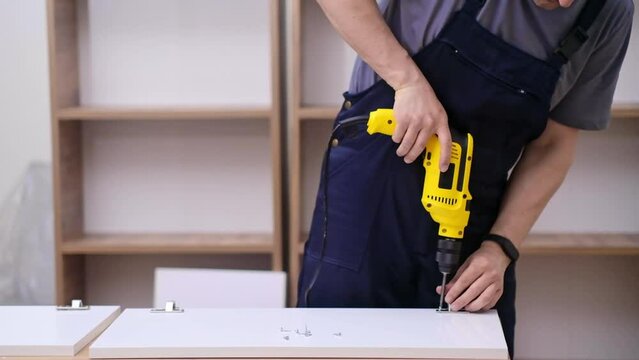 Furniture delivery and installation handyman in coveralls using screwdriver to fix hinge on wooden cabinet door specialist working with professional equipment