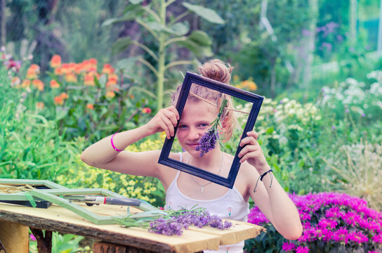 girl holding and showing wooden frame with lavender bouquet in it, outdoors in colorful garden