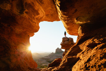 Horizontal image woman standing at dramatic viewpoint at Merry-go-round Rock in Sedona Arizona at sunset with sun flare admiring the landscape view.