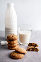 On a gray table is a blurry image of a cookie, a cup and a bottle of milk.