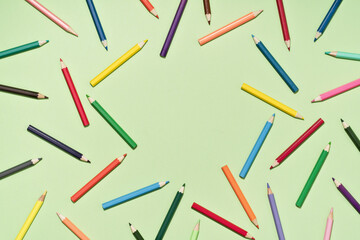 Colored Pencils background pattern on light green. Back to School or drawing and creativity concept. Copy space in center. Top view