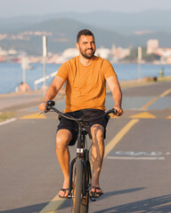 Carefree man with bicycle riding at sunset having fun and smiling