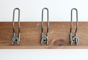Three metal coat hooks on wooden panel attached to white wall
