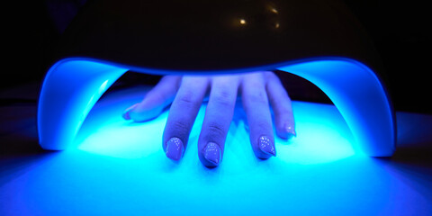 Woman's hand inside lamp for drying nail polish on table close-up. UV lamp for drying nail polish