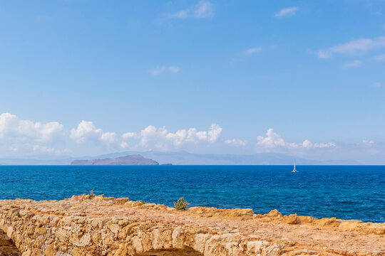 Ruins of a fortress on the shores of the mediterranean sea. White sail on the horizon