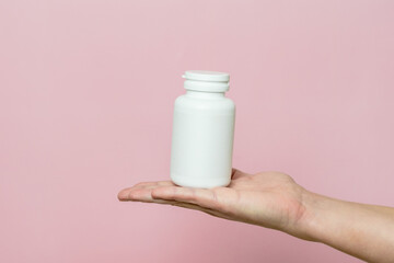 Woman's hand holding bottle of pills or vitamins. White packaging for your pill or capsule and supplement