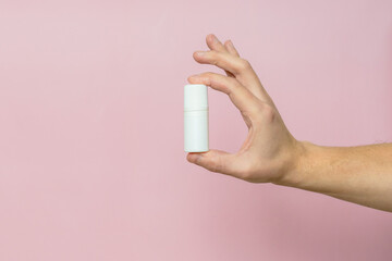 Drops bottle for eye or ear in hand on pink background. Pharmaceutical product. Copy space.