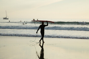 Silhouette Of surfer people carrying their surfboard on sunset beach. Surfer sport and travel concept.