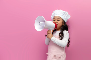 little Asian girl in chef uniform announces news and information with megaphone on pink isolated...