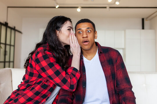 Young European Woman Telling Secret To African American Man, Wife Whispering In Ear To Husband And Hinting