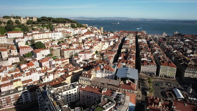 Aerial drone orbit of Baixa District in Lisbon, Portugal with major landmarks visible including Rossio Square, St. George Castle and 25 April Bridge