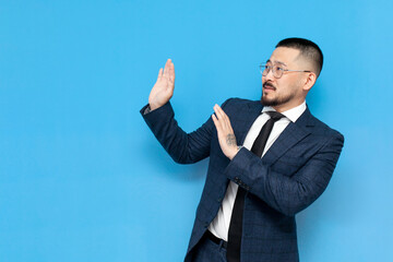 successful Asian businessman in suit and glasses refuses and avoids copy space on blue isolated background
