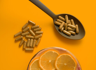 kratom pills composition on orange background with kratom filled spoon, top view, flat lay