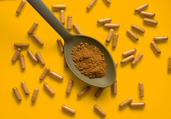 kratom pills composition on orange background with kratom filled spoon, top view, flat lay