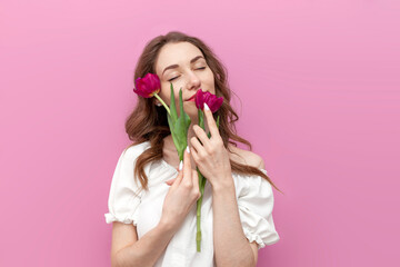young tender girl touches the skin of her face with two pink tulips and smells the smell on pink...