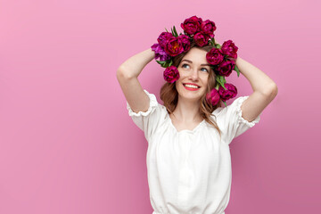 young tender girl with pink tulips in her hair thinks and dreams on pink isolated background, woman with flowers