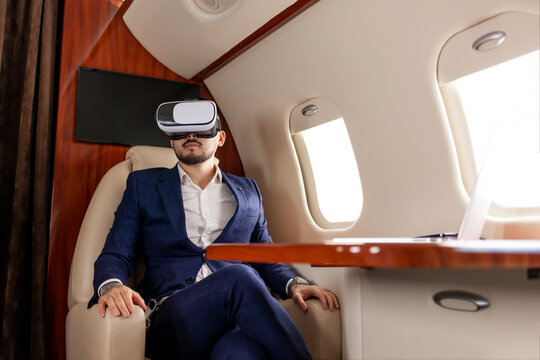 businessman in suit flies in private plane in virtual reality glasses and presses with his hands on imaginary interface