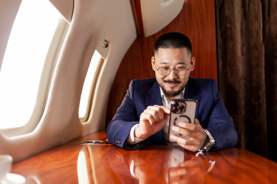 Asian businessman is flying in private luxury jet and using smartphone, Korean entrepreneur typing on phone