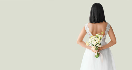 Beautiful young Asian bride with bouquet of eustoma flowers on light background with space for text, back view