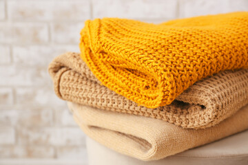 Pouf with beautiful sweaters near brick wall in room, closeup