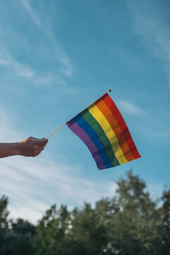 Vertical cropped image of an unrecognizable young woman's hand waving a rainbow flag banner. LGTBIQ+ Concept