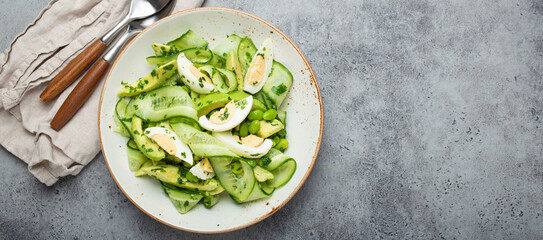 Healthy green avocado salad bowl with boiled eggs, sliced cucumbers, edamame beans, olive oil and...