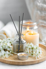 Obraz na płótnie Canvas Home comfort, coziness, aromatherapy. Cozy interior with knitting, burning candles and aroma perfume diffuser in the living room. Fresh spring blossom fragrance, apple cherry flowers.