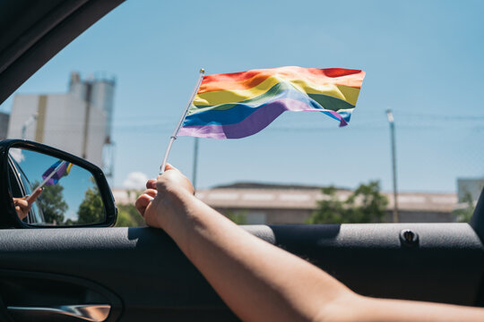 Hand of unrecognizable person waving a rainbow flag out of a car window. LGTBIQ+ Concept