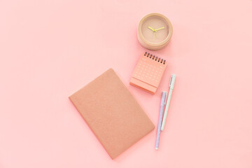 Flip paper calendar with alarm clock and notebook on pink background