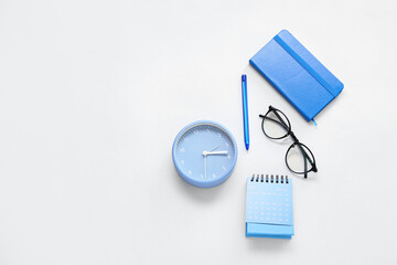 Flip paper calendar, alarm clock, eyeglasses and notebook on blue background