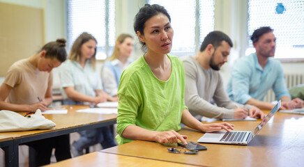 Fototapeta premium Asian girl is a student engaged on a laptop during classes, studying in a university auditorium with a group