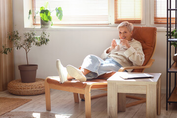 Mature woman with cup of tea resting on armchair at home