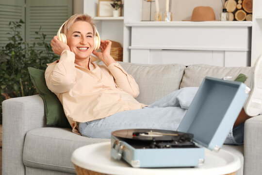 Mature woman with headphones and record player listening to music on sofa at home