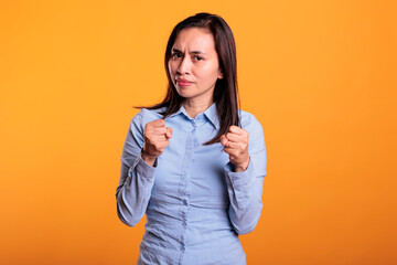 Aggressive filipino fighter doing self defense gesture in studio standing over yellow background. Defensive woman clenching fists ready to punch, expressing anrgy reaction preparing boxing
