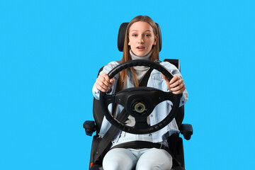 Shocked female student with steering wheel in car seat on blue background