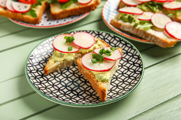 Plates with delicious radish bruschettas on green wooden table