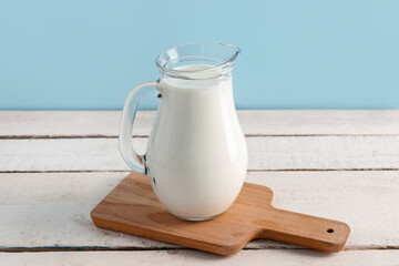Jug with fresh milk on white wooden table