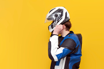guy motorcyclist in leather jacket puts on helmet on yellow isolated background, professional racer in protective gear
