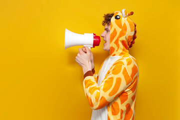 young joyful guy in funny children's giraffe pajamas speaks into megaphone and points his hand to the side