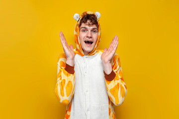 young joyful guy in funny baby giraffe pajamas holds his hands in front of him on yellow background
