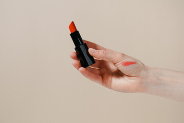 Female hand holding red lipstick with swatch on beige isolated background. Concept of decorative cosmetics, beauty and aesthetics