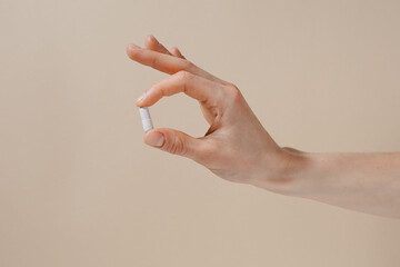 Female hand holding white pill with fingers on beige isolated background. Concept of health care, dietary supplements, treatment of depression and diseases